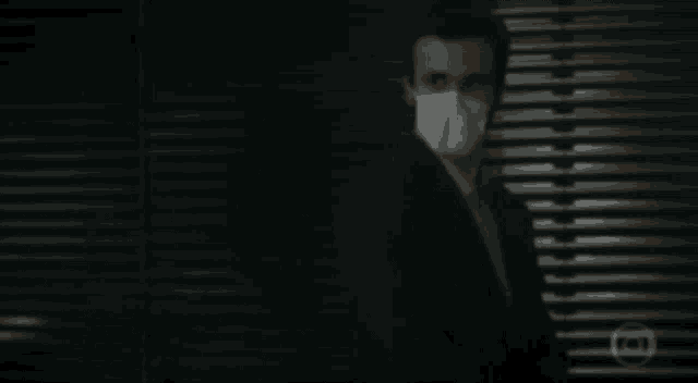 a man wearing a face mask is standing in front of a window .