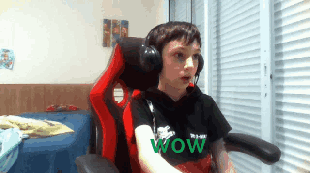 a boy wearing headphones and a wow shirt sits in a red chair