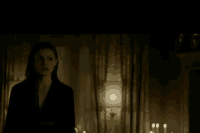 a woman stands in a dark room with candles and a lamp