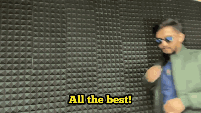 a man wearing sunglasses is dancing in front of a wall that says all the best !