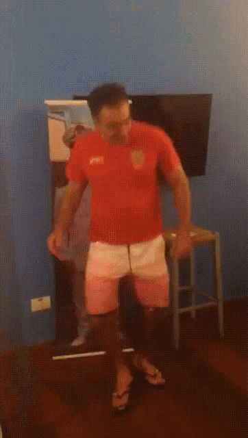 a man in a red shirt and white shorts is dancing in front of a blue wall