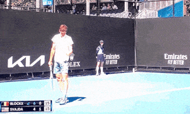 a man holding a tennis racquet on a tennis court with emirates fly better advertisements behind him
