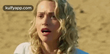a woman with blonde curly hair is making a funny face while standing on a beach .