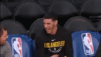 a man in a los angeles shirt is sitting in a basketball stadium .
