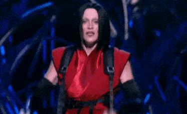 a woman in a red shirt and black gloves is making a face on a stage .