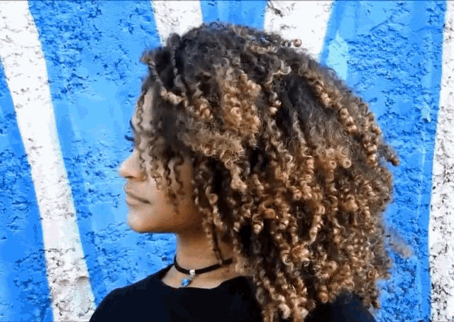 a woman with curly hair stands in front of a blue and white striped wall