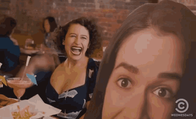 two women are laughing in a restaurant with a wednesdays logo on the bottom left