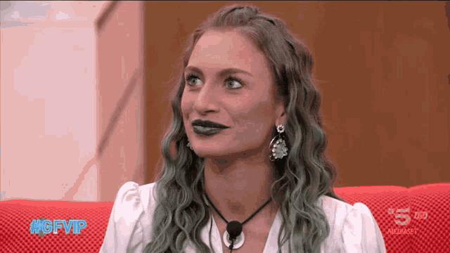 a woman with green hair is sitting on a red couch with #gfvip written on the bottom
