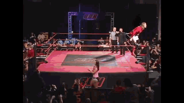 a woman in a pink shirt is standing in a wrestling ring with a referee .