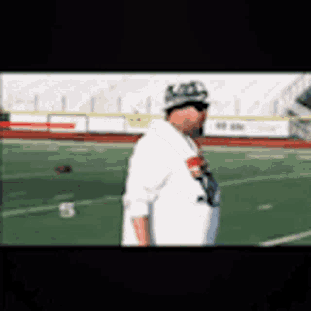 a man wearing a hat and sunglasses is walking on a football field