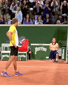 a man in a yellow shirt stands on a tennis court in front of a perrier advertisement