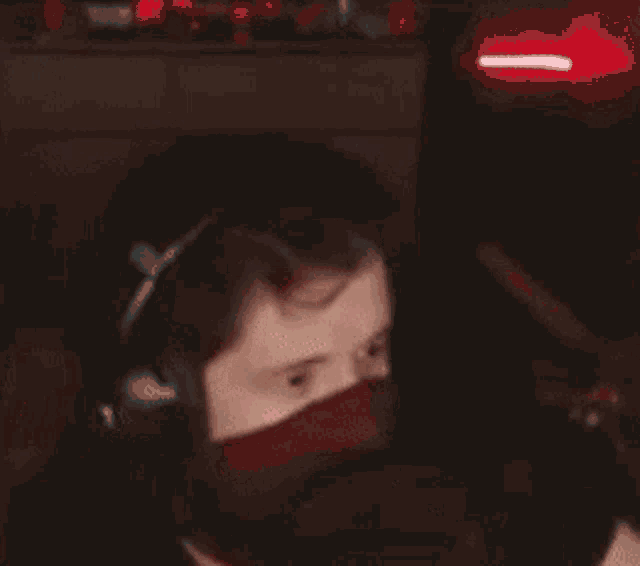 a person is covering their face with their hands in a dark room with a red light behind them .