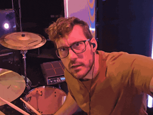 a man wearing glasses and ear buds playing drums