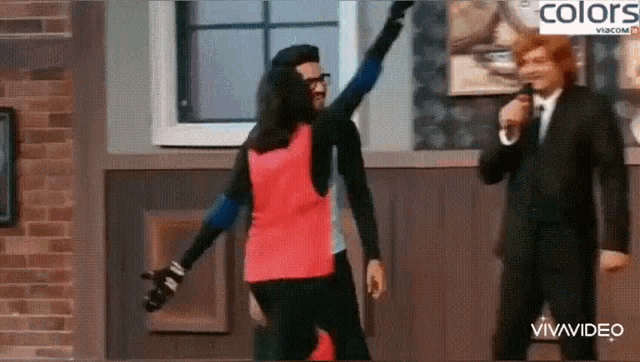 a man in a suit is talking into a microphone while a woman in a red jacket is dancing .