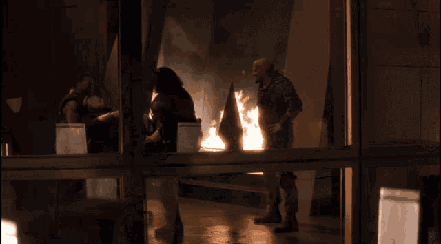 a group of men standing in front of a window with a fire in the background