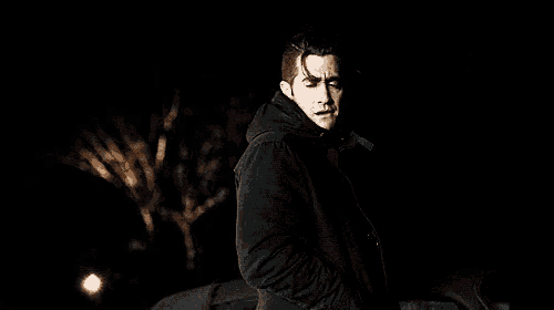 a man in a black coat is standing in the dark in front of a car .