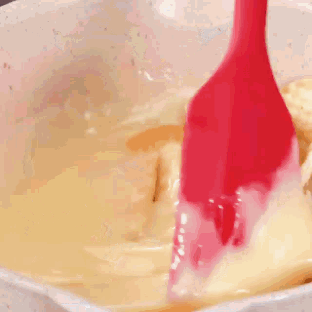 a red spatula is being used to stir a casserole dish filled with food