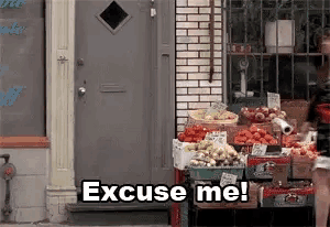 a person is standing in front of a fruit stand and says excuse me .