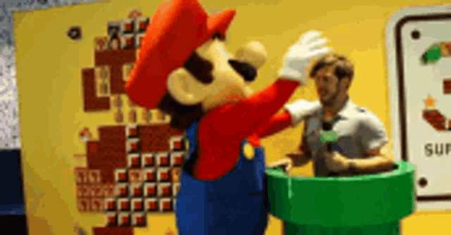a mario mascot is standing next to a green pipe