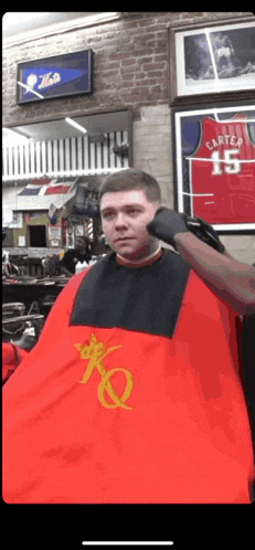 a man is getting his hair cut by a barber wearing a red cape with the letter k on it