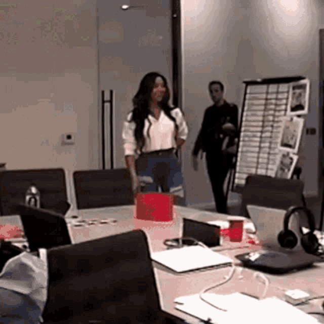 a woman in a white shirt is standing in a conference room with a red box on the table