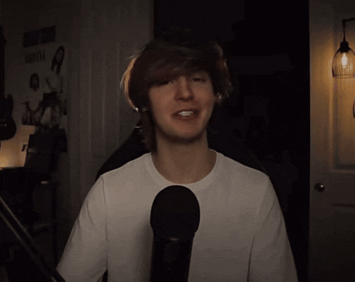 a young man stands in front of a microphone in a dark room