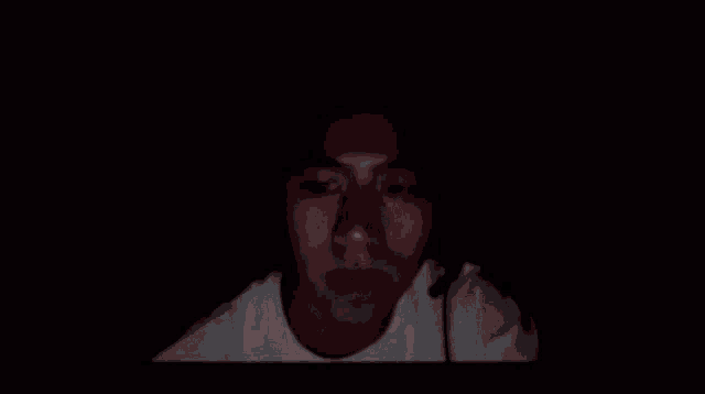 a man in a white shirt is holding his head in his hands in the dark .