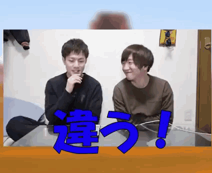 two men are sitting at a table with a blue sign that says ' ! '