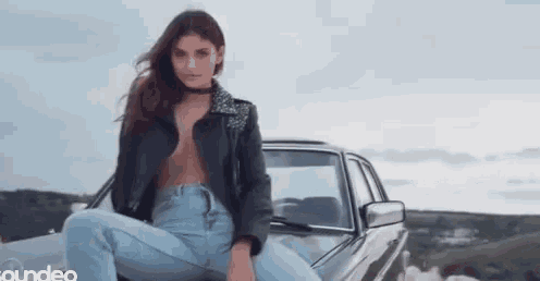 a woman is sitting on the hood of a car with her legs crossed .
