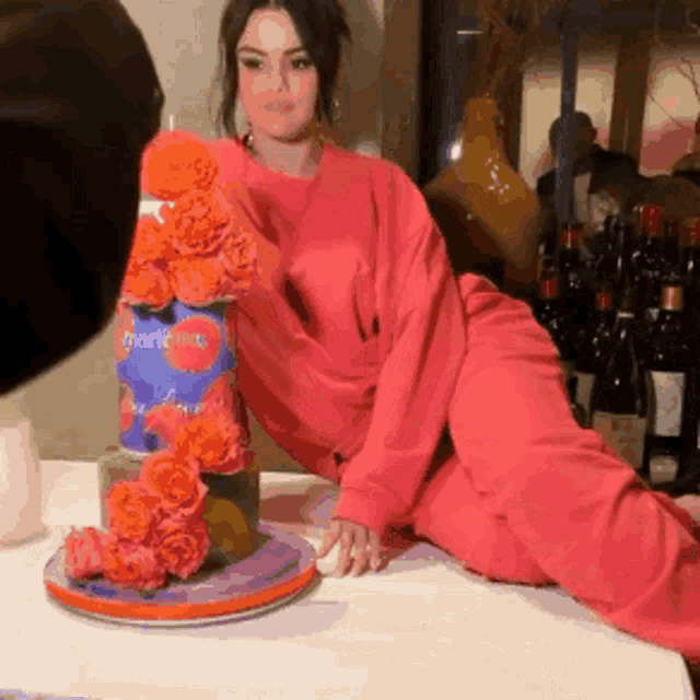 a woman in a pink sweater sits next to a cake that says thank you