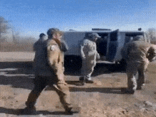 a group of soldiers are walking down a dirt road in front of a van .