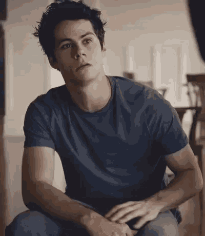 a young man in a blue t-shirt is sitting on a couch in a living room .