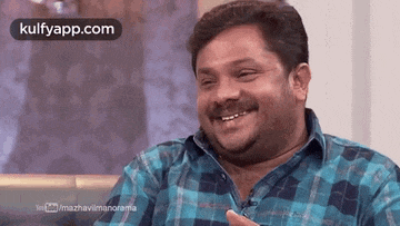 a man in a plaid shirt is smiling and laughing while sitting on a couch .