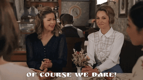 two women sit at a table with the words of course we dare on the bottom