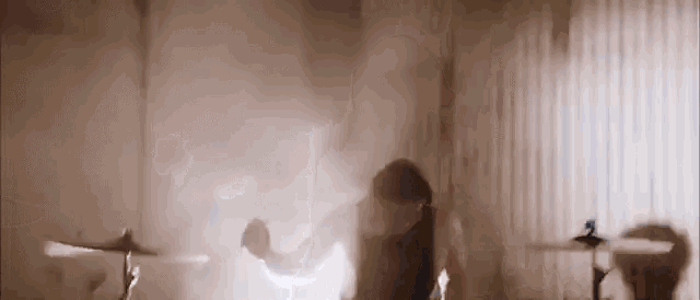 a woman is dancing in a room with a drum set in the background .
