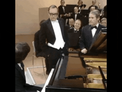 two men in tuxedos are standing next to a piano