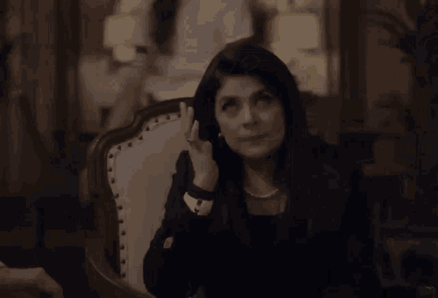 a woman sits in a chair with her hand on her face