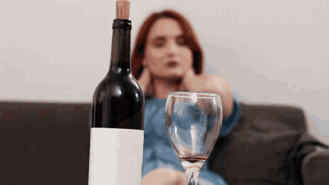a woman sits on a couch with a glass of wine and a bottle of wine