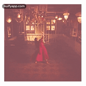 a woman in a red dress is dancing in a hallway with a chandelier .