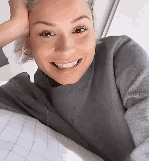a woman in a grey sweater is smiling and laying on a bed