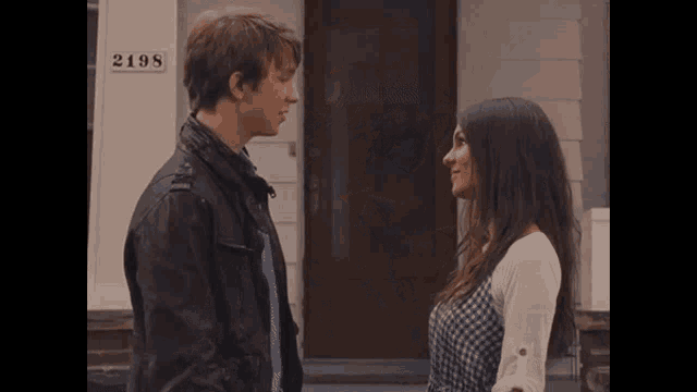 a man and woman are looking at each other in front of a house with the number 2098