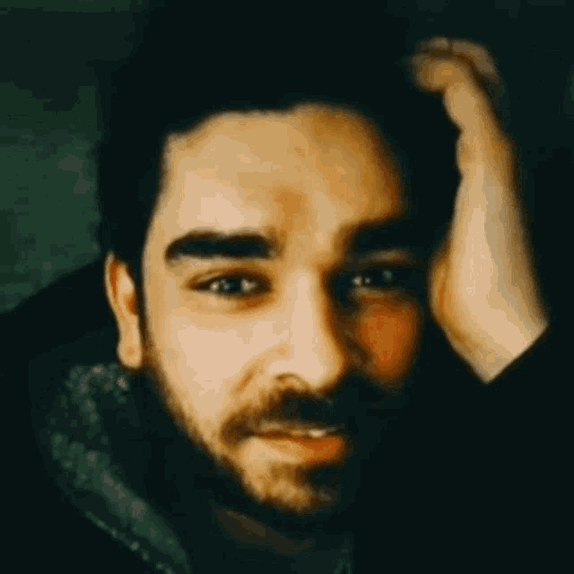 a man with a beard holds his hand to his forehead