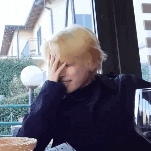 a person with blonde hair is covering their face with their hand .