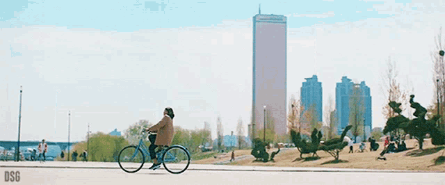a woman is riding a bike in a park with a large building in the background ..