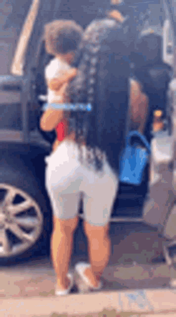 a woman is standing next to a car holding a child .