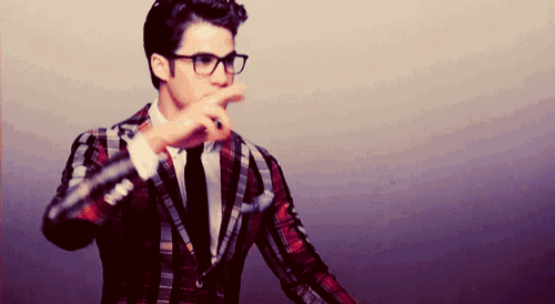 a man wearing glasses and a plaid suit is pointing