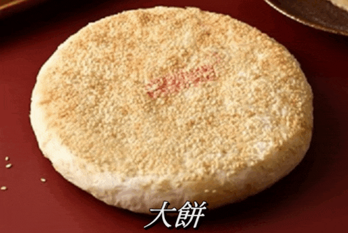 a round bread with sesame seeds on it is on a red surface