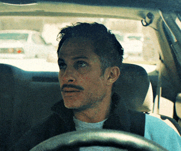 a man with a mustache sits in a car