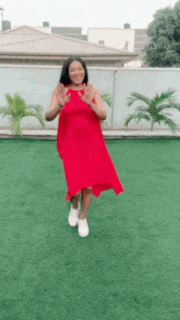 a woman in a red dress and white shoes is standing on a green field .