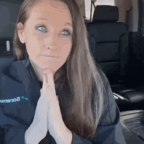 a woman is sitting in the back seat of a car with her hands folded in front of her face .
